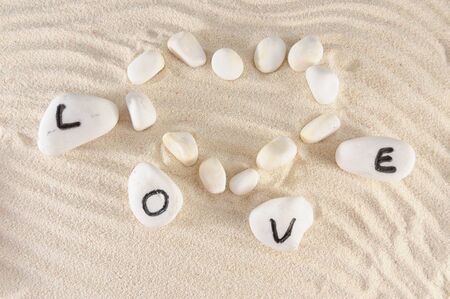 Love word and heart shape on group of stones with sand as backgroundの写真素材
