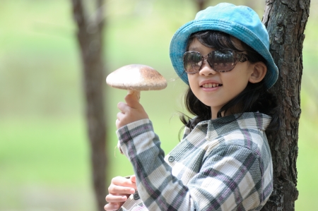 Asian kid holding a mushroom and sitting against a treeの写真素材