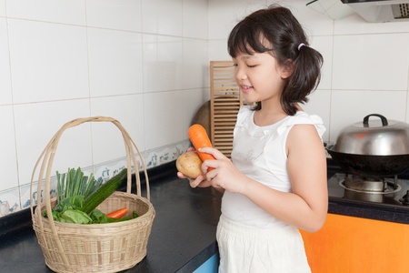 Asian kid holding carrots in the kitchenの写真素材