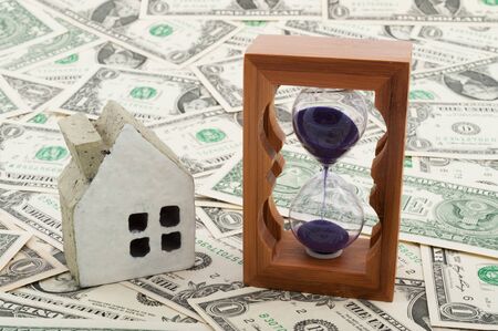 House model and hourglass on piles of paper moneyの写真素材