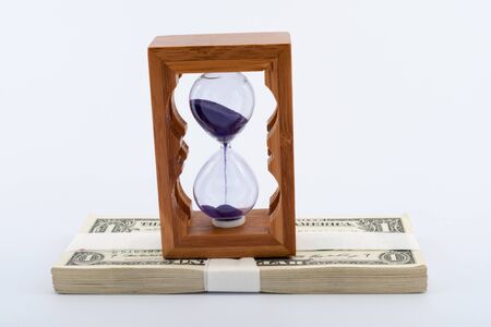 Hourglass on pile of paper money over  white backgroundの写真素材