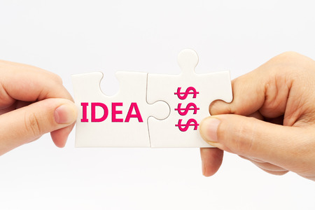 Two hands holding puzzle pieces which written Idea and money wordsの写真素材