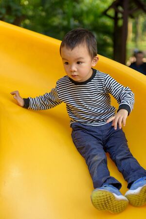 Asian kid playing on the slide in the parkの写真素材