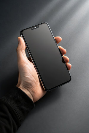 male hand holding a smartphone with a black screen on a dark backgroundの素材