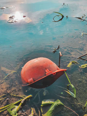 Orange builder safety helmet lies in the water on river bank. Vertical orientationの写真素材