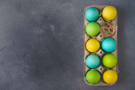 Bright colorful easter eggs in egg carton on grey background. Top view, Copy space