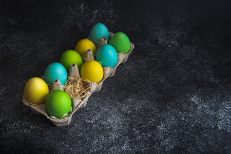 Colorful painted easter eggs in egg carton decorated with shavings on black background. Copy spaceの写真素材