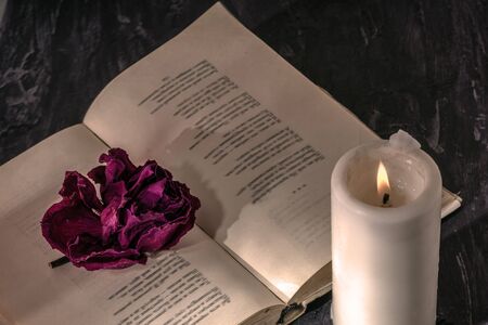 an open book with a candle. on the pages is a Bud of dried rose.の写真素材