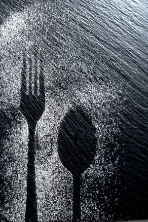 Spoon and fork silhouette made with flour on dark texture background, up vertical viewの写真素材