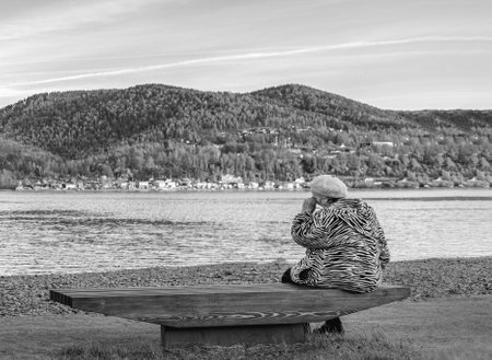 Krasnoyarsk, Russia, July 29, 2019: the old grandmother is sad and crying on the Bank of a beautiful river. black and white dramatic photoのeditorial素材