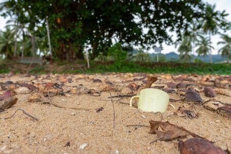 an old Cup lies on the sand. garbage on the beach in Thailandの写真素材