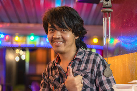 Khaolak, Thailand, 5 june 2019: Thai guy, a young man in a plaid shirt happy and cheerful. he holds his finger up and smiles. at night on the background of a nightclubのeditorial素材
