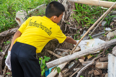 Khao Lak, Thailand, 1 june 2019: Asian boy student boy scout volunteer removes debris and clean the beach from dirt and waste on the international day of environmental protectionのeditorial素材