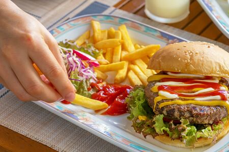 female hands fingers holding and dripping fried French fries in tomato ketchup on a plate with...