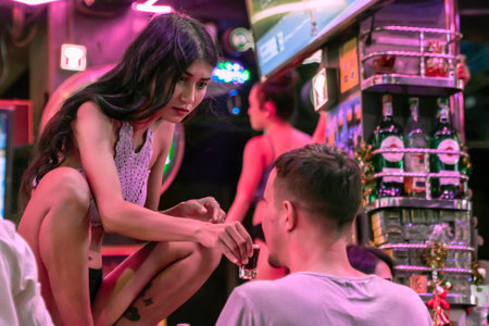 Thailand, Phuket, Patong 3 January 2020: the stripper gives a shot of whiskey or vodka to a young man who visits a strip bar. Nightlife and sex tourism in Thailandのeditorial素材