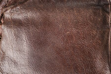 brown background-leather fabric, close-up leather with a reddish tint. Old, stylish, worn. Beautiful texture for designers, design and layouts, Seam, thread and stitch, visible scuffs and scratches,の写真素材