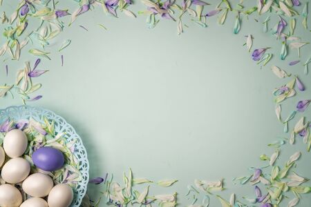 Easter eggs and colorful petals of spring flowers on a light green background. Copy space.