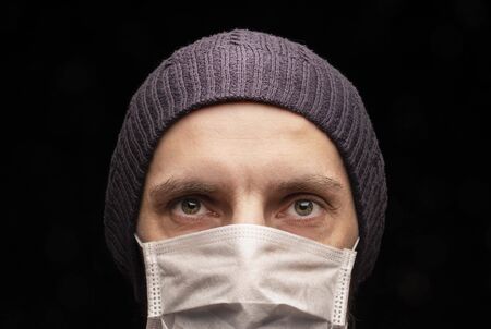 The man in the cap at the medical protective mask, anti-infectious, protection against coronavirus. Intense stare at the camera , close- up, eyes, stern look. Male brutal portrait. Pandemic epidemicの写真素材