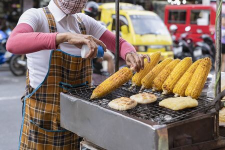 the cook sprinkles salt on freshly cooked grilled corn. street food in Asia , Thailand