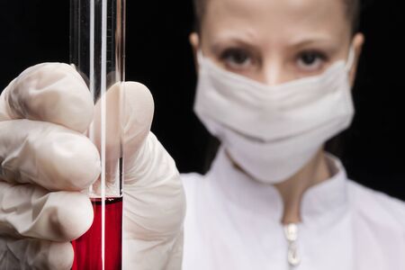 a test tube with a red blood test in the hands of a medical worker in a medical mask. girl doctor in blur. close-up, lookの写真素材