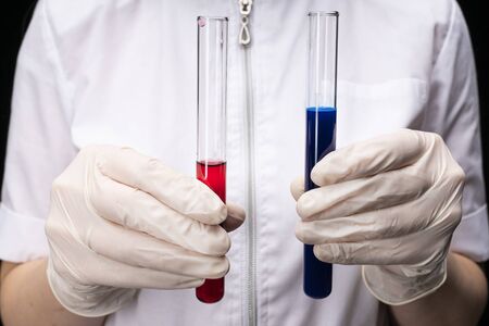 two vials of blue and red liquid, in gloved hands against the background of a medic. development of...