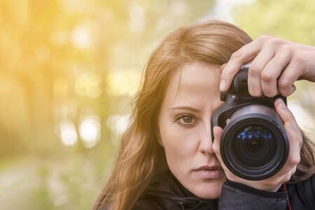 photographer girl, close-up portrait. The girl model takes photos, looking at the viewer and into the lens of the outdoor camera. red hair develop, copyspaceの写真素材