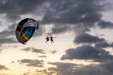 people ride, fly on a parachute along the coast over the sea against the background of a wonderful sunset. Attraction entertainment for tourists in the sea resorts of Thailand, Asia and around the world.の写真素材