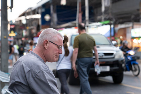 Thailand, Phuket, April 15, 2020: a white-haired European man is sitting on his face and drinking beer. close-up portrait, real life, street photo on Bangla roadのeditorial素材