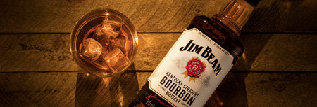 Russia, Krasnoyarsk, July 28, 2020: a bottle of Jim beam Bourbon from Kentucky and a glass of ice on a light brown wooden background. panoramic picture.のeditorial素材