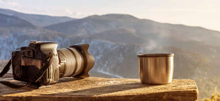 Minimalistic still life in the mountains panorama-camera and steaming mug thermos with hot tea or...