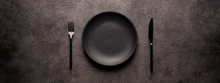 black empty plate and cutlery, fork and knife, on a dark textured background. Mockup concept for the...