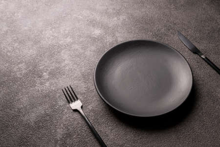 empty black plate, fork and knife on a dark background, horizontal photoの写真素材