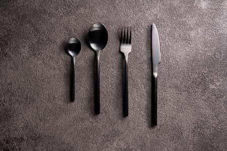 Black cutlery-fork, spoon, knife, on a dark background in the center. Minimalistic flat lay still lifeの写真素材