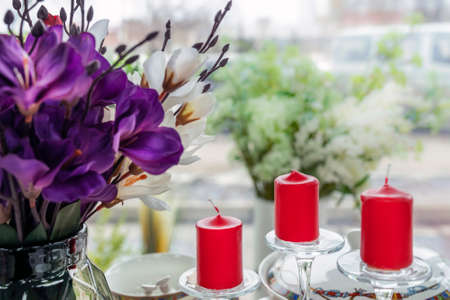three red candles on the background of the window, a purple bouquet of flowers and decor