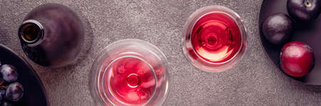 a bottle of red wine and flatlay glasses. plums on a textured table are gray concrete, a header for...