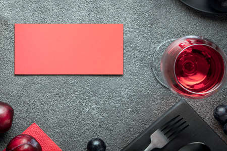 A glass of wine and a red postcard on a gray concrete table. An invitation to a restaurant for a...