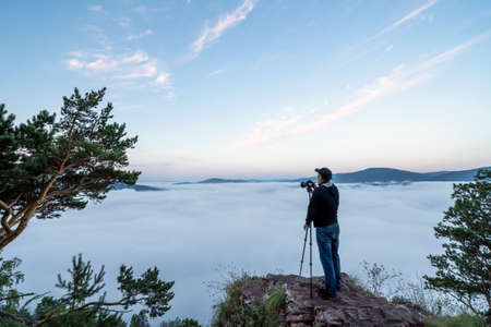 a man photographer in the mountains takes pictures with a camera on a tripod of nature and the...