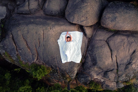 a young beautiful girl in the mountains on a snow-white sheet, top view, aerial photo from a drone. comfort and comfort, a craving for consolation and adventure, but with clean bed linenの写真素材