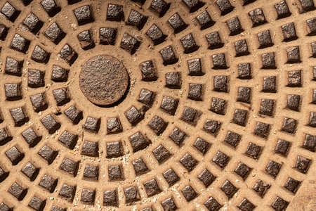 a metallic texture made of bronze cubes depicting the sun and rays radiating from it. a fragment of a sewer manholeの写真素材