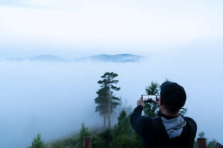 thick fog and a gloomy morning in the forest on a mobile phone camera. a tourist traveler takes pictures of nature on a smartphone camera. a middle-aged man is a lover of hiking, social networksの写真素材