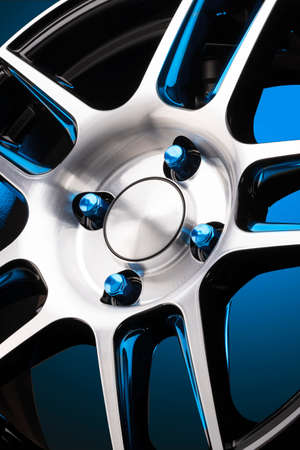 close-up of an alloy wheel and blue wheel nuts on a gradient blue background. aluminum wheel details, beautiful shiny wheel spokes on a black background vertical photoの写真素材