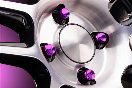 beautiful bright automotive seven-sided wheel nuts purple close-up on a sporty style alloy wheel on a black background for auto tuning of a tire and disk store or auto parts gradient purple red background.の写真素材