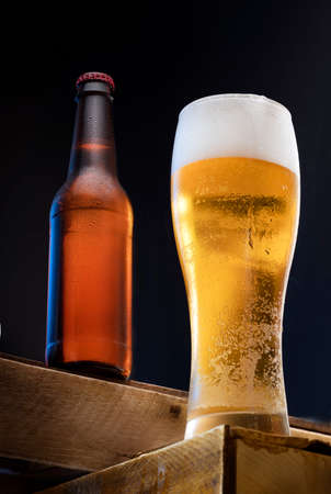 a glass of cold fresh light beer and a bottle of steamed cold beer in the background on a black background. a party or celebration in a beer restaurantの写真素材