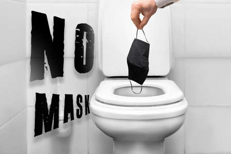 the end of quarantine and pandemic. a mans hand throws a protective medical mask against into the toiletの写真素材