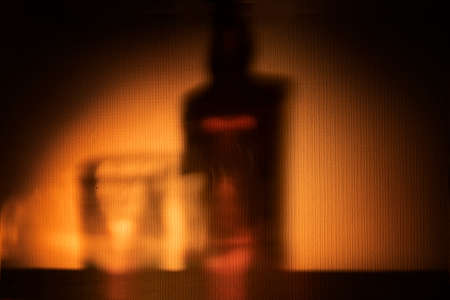 abstract background - yellow orange shadow from a bottle of brandy whiskey or rum on the wall . alcoholic drinks in a cozy atmosphere at the bar or at home. party and drinksの写真素材