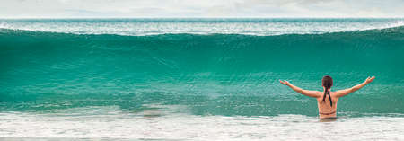 the girl dives into a large oncoming wave. Beautiful turquoise water background, vacation and fun by...