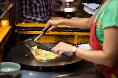 thai chef woman flips pancakes. close-up frying fast food on the street in the eveningの写真素材
