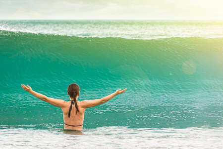 A woman bathing in the sea, with her arms outstretched, meets a powerful oncoming wave. Fun on the beach and a tropical vacation. Copy space background on the rightの写真素材