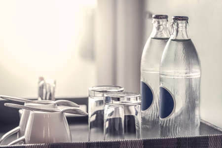 two bottles of mineral water in the hotel room, as well as clean glasses on a tray, light from the windowの写真素材