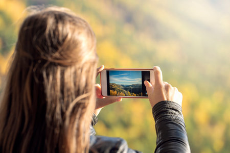 a young woman takes pictures of nature on a smartphone, a view from the back. active lifestyle and...